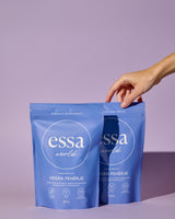 A hand grabbing one of two full-size Essa World vegan proteins in choco-spice flavour in front of a purple background.